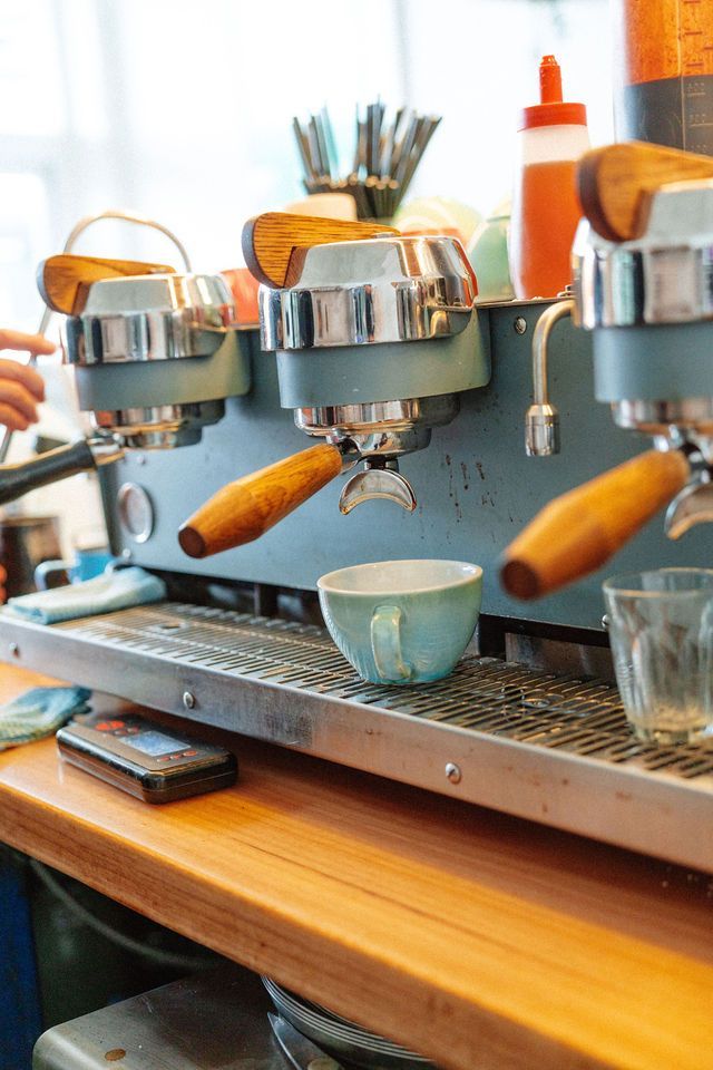 A coffee machine is sitting on a wooden counter next to a cup of coffee.