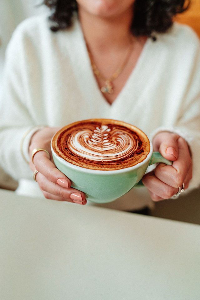 A woman is holding a cup of cappuccino in her hands.