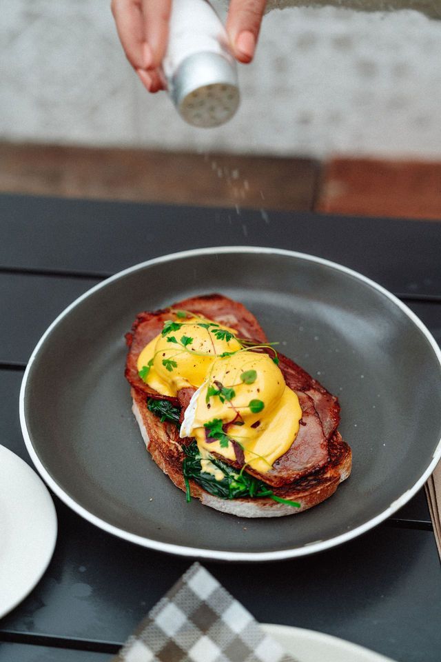 A person is salting a plate of food with a salt shaker.