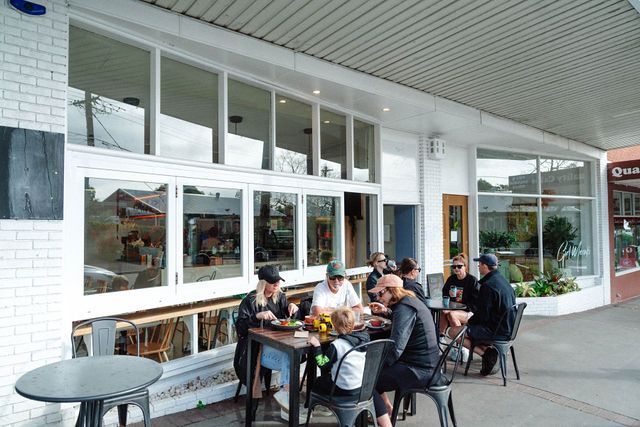 A group of people are sitting at tables outside of a restaurant.