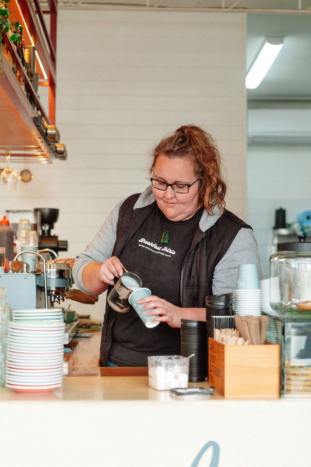 A woman is pouring milk into a cup of coffee.