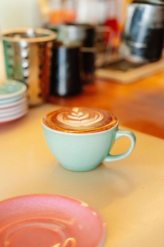 A cup of cappuccino is sitting on a table next to a pink saucer.