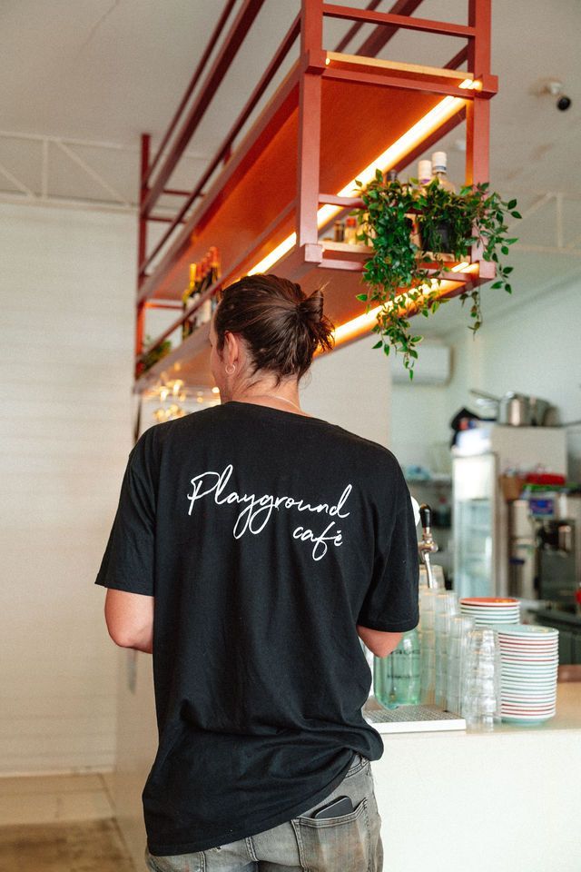 A man wearing a black t-shirt is standing in front of a counter in a restaurant.