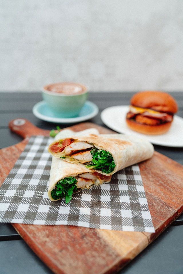 A chicken wrap is sitting on a checkered napkin on a wooden cutting board.