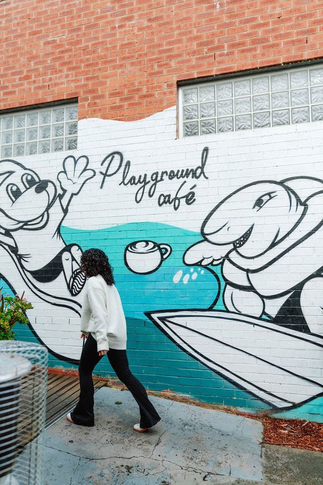 A woman is walking past a mural of a dog and a shark on a brick wall.