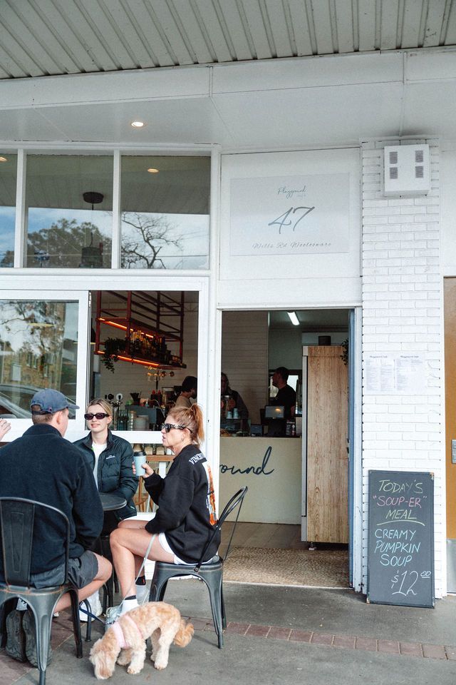 A group of people are sitting outside of a restaurant with a dog.