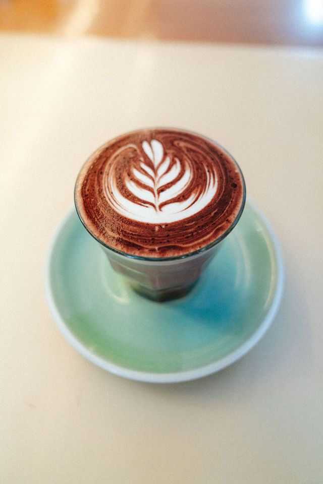 A cup of cappuccino with latte art on a saucer on a table.