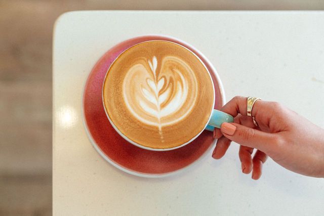 A person is holding a cup of cappuccino on a table.