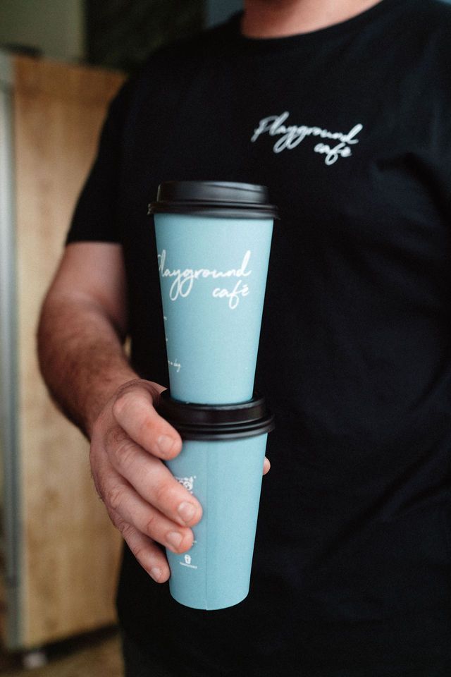 A man in a black shirt is holding two cups of coffee.