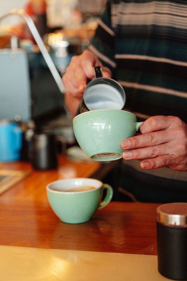 A man is pouring milk into a green cup of coffee.