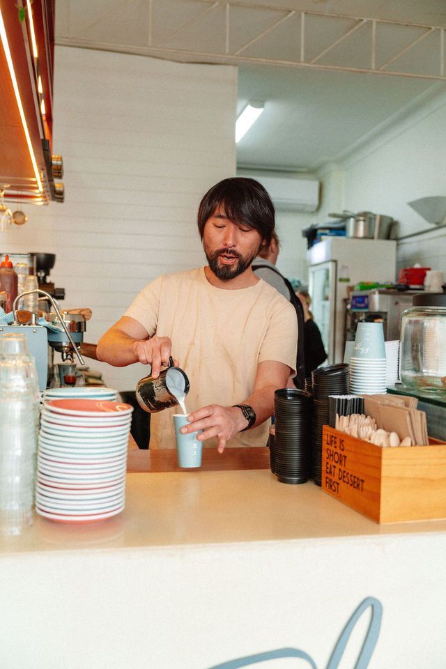 A man is pouring milk into a cup of coffee.