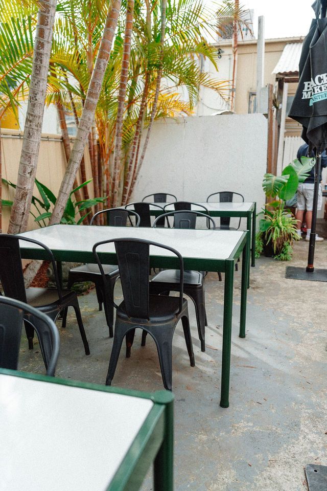 A row of tables and chairs in a courtyard with trees in the background.