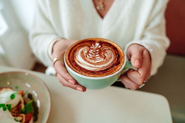 A woman is holding a cup of cappuccino in her hands.