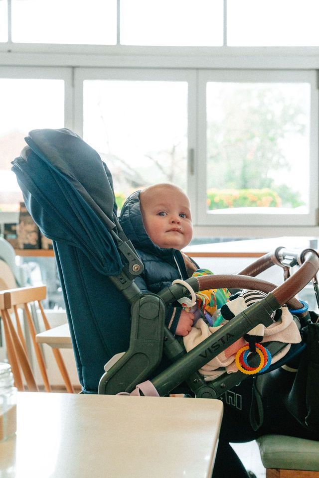 A baby is sitting in a stroller at a table.