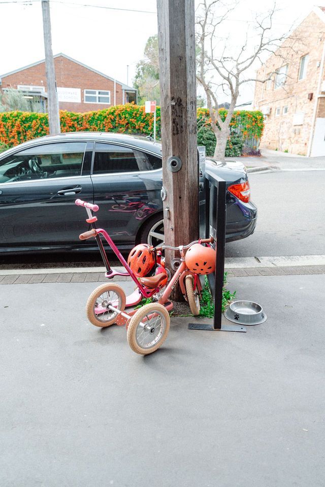 A pink tricycle is parked on the side of the road next to a car.