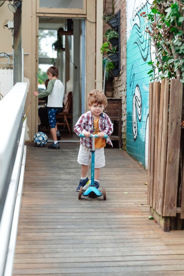 A young boy is riding a scooter down a wooden walkway.