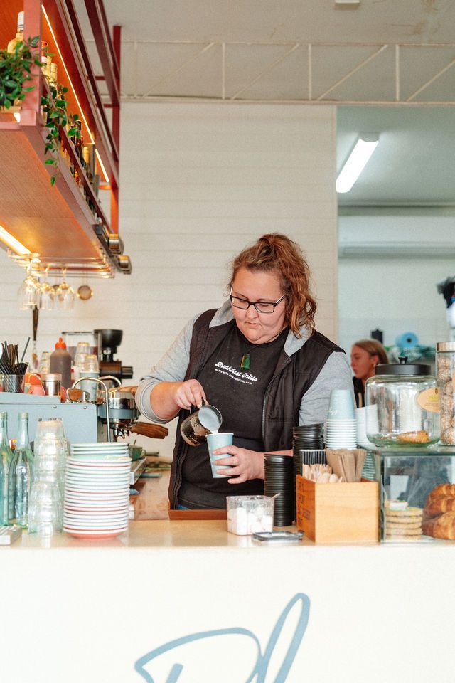 A woman is pouring milk into a cup of coffee.