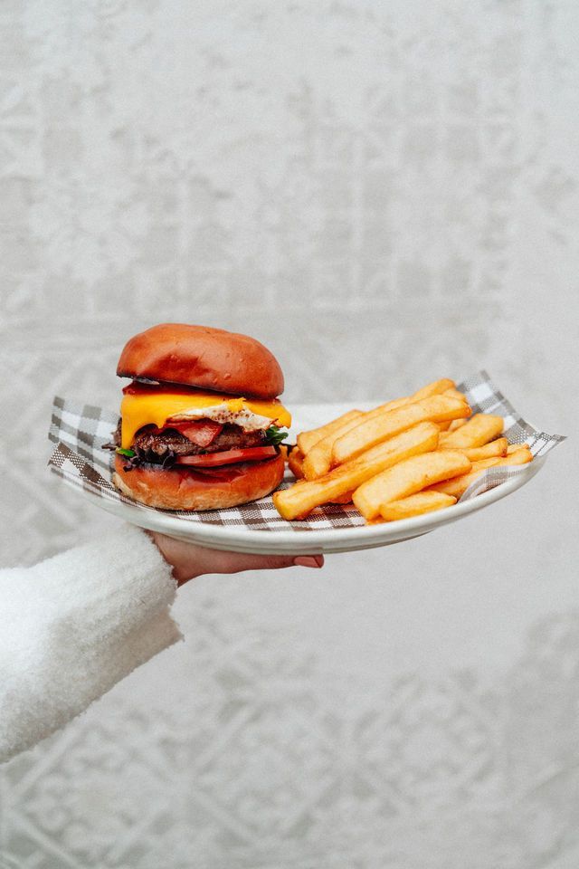 A person is holding a plate with a hamburger and french fries on it.