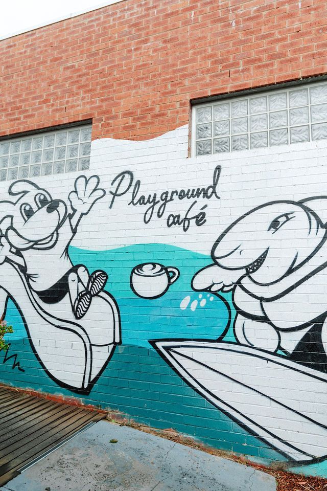 There is a mural on the side of a building that says playground cafe.