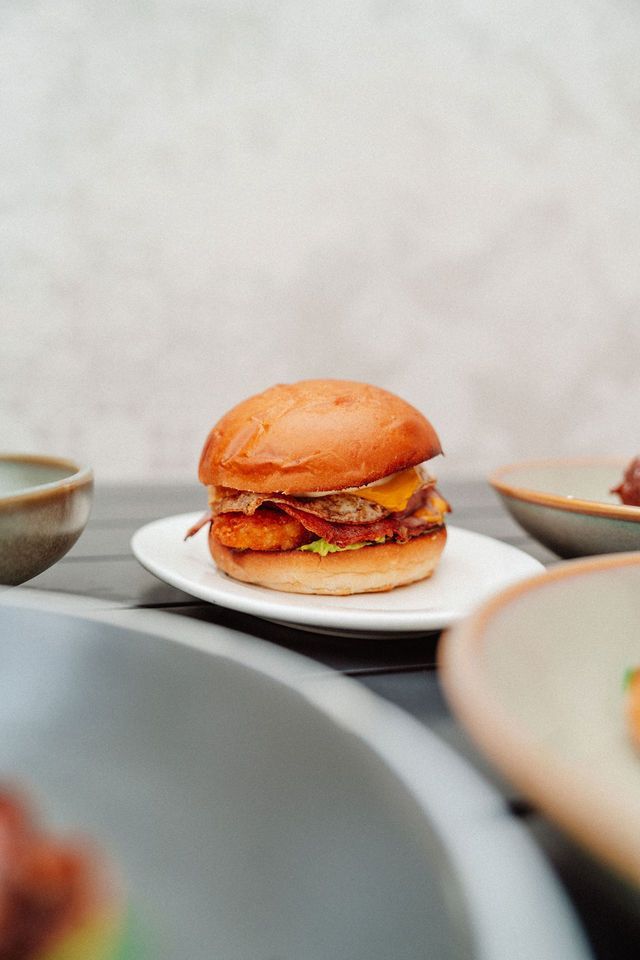 A hamburger is sitting on a white plate on a table.