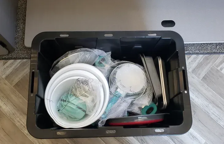 A black plastic bin filled with buckets , pans , and utensils.