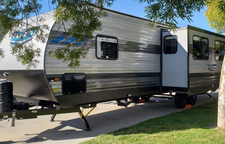 A travel trailer is parked in a driveway next to a tree.