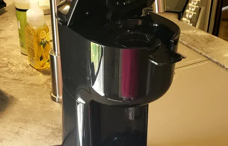 a black coffee maker is sitting on a counter next to a faucet .