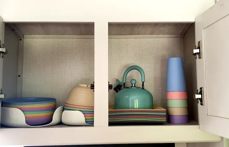 a kitchen cabinet filled with bowls , cups , and a tea kettle .