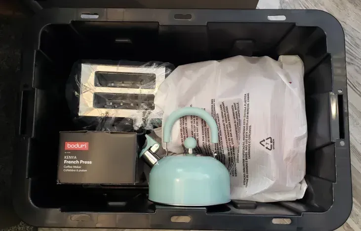 A black plastic container filled with a tea kettle and a toaster.