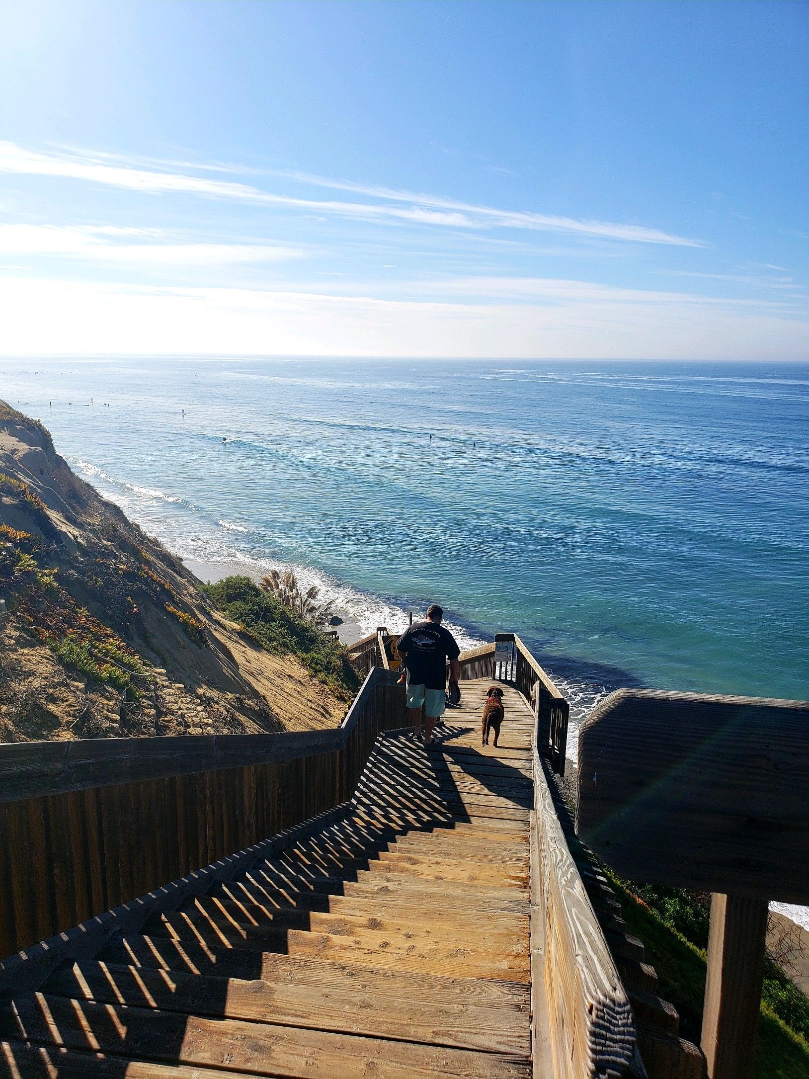a person is walking down a set of stairs towards the ocean .