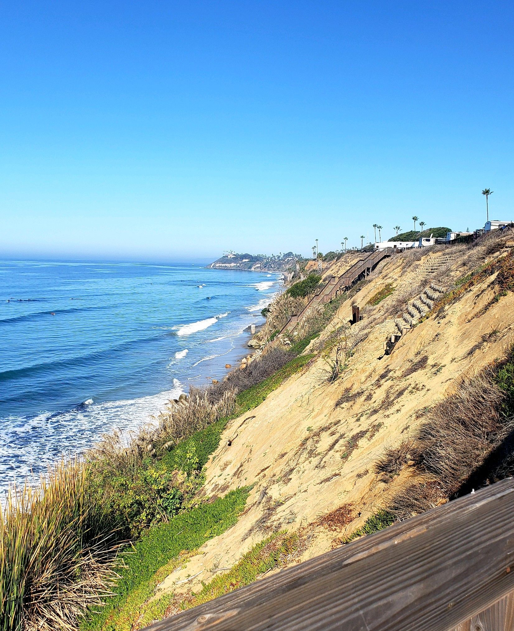 a cliff overlooking the ocean with a wooden fence in the foreground .