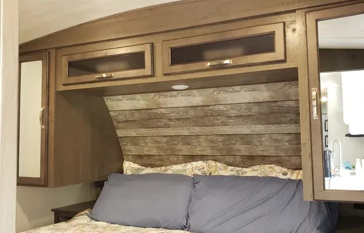a bedroom with a bed , cabinets , mirrors and a wooden headboard .