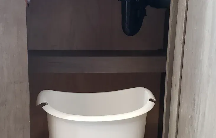 A white trash can is sitting under a sink in a bathroom.