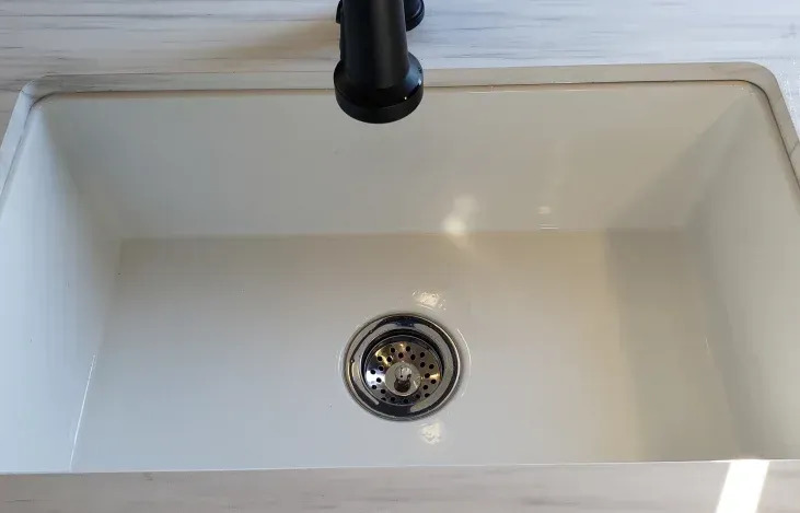 A white kitchen sink with a black drain and faucet.