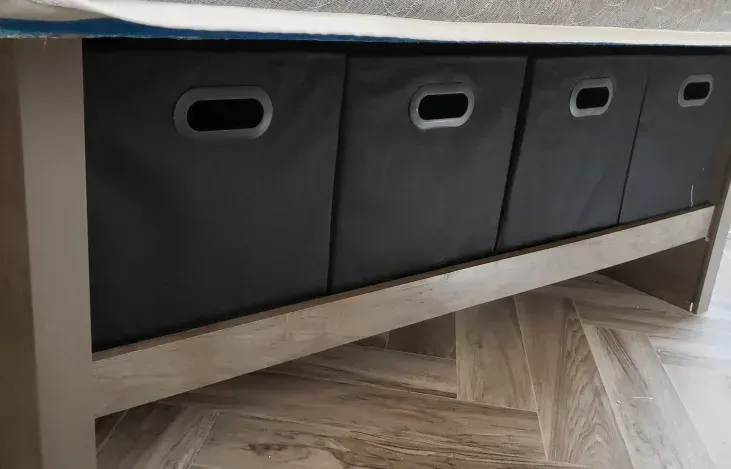 A wooden bench with three black bins underneath it.