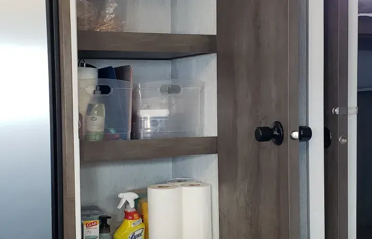 A kitchen cabinet filled with cleaning supplies and paper towels.