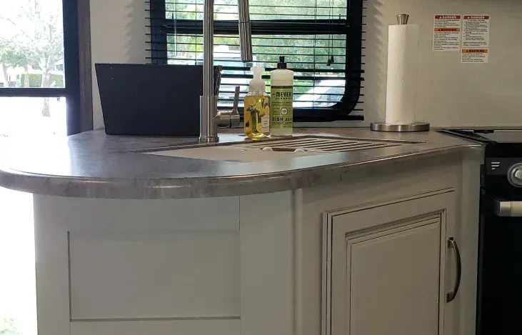 A kitchen with a sink , stove , and a laptop on the counter.