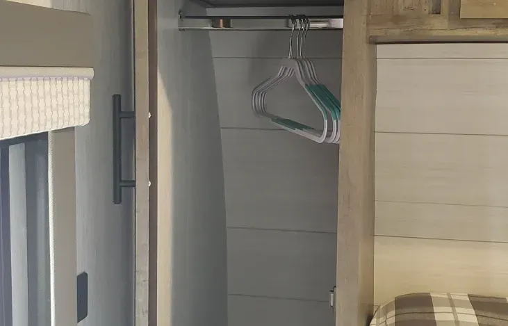 A closet with clothes hanging in it and a bed in the background.