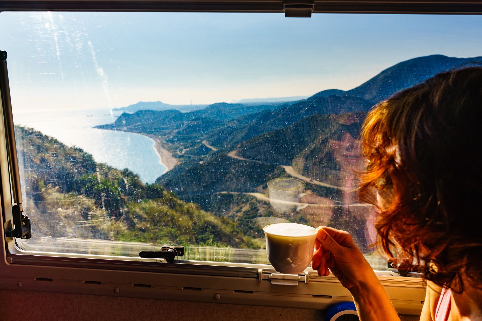 a woman is sitting in a camper drinking coffee and looking out the window . a woman is sitting in a camper drinking coffee and looking out the window .