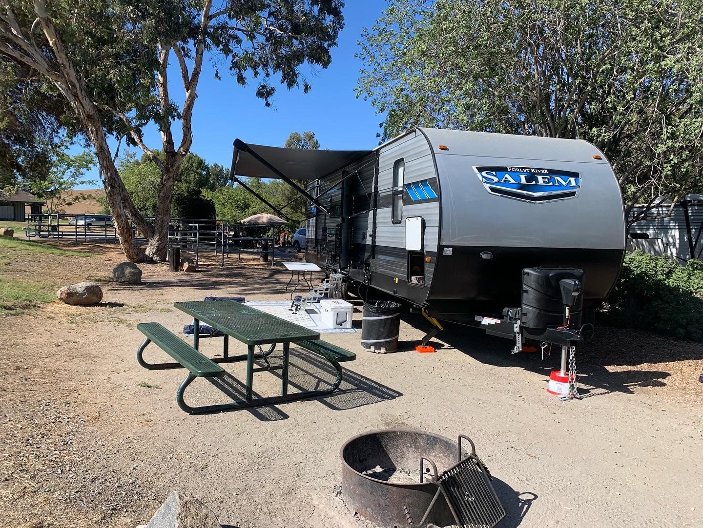 a trailer is parked in a campground with a picnic table and a fire pit .