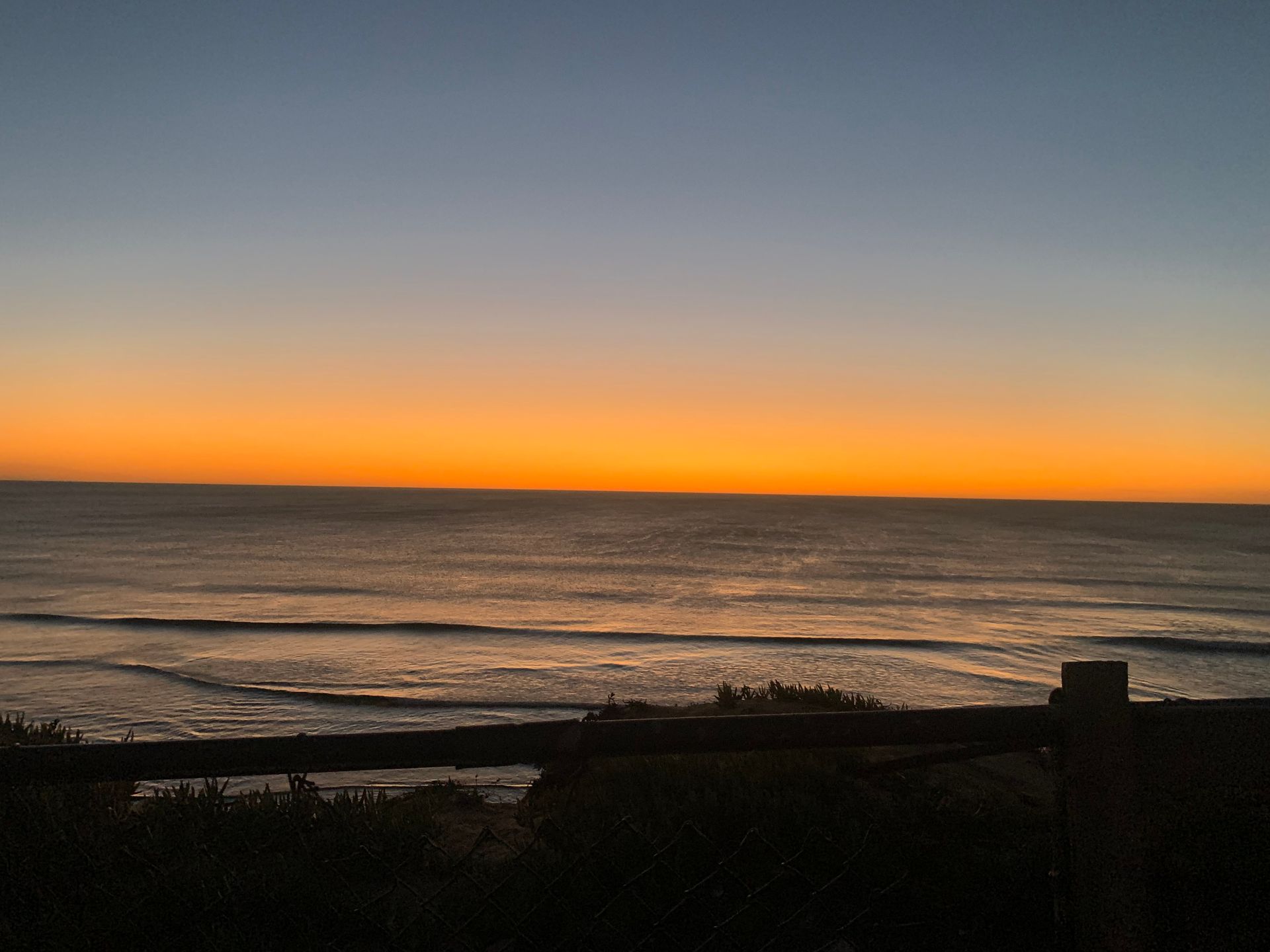 a sunset over the ocean with a fence in the foreground