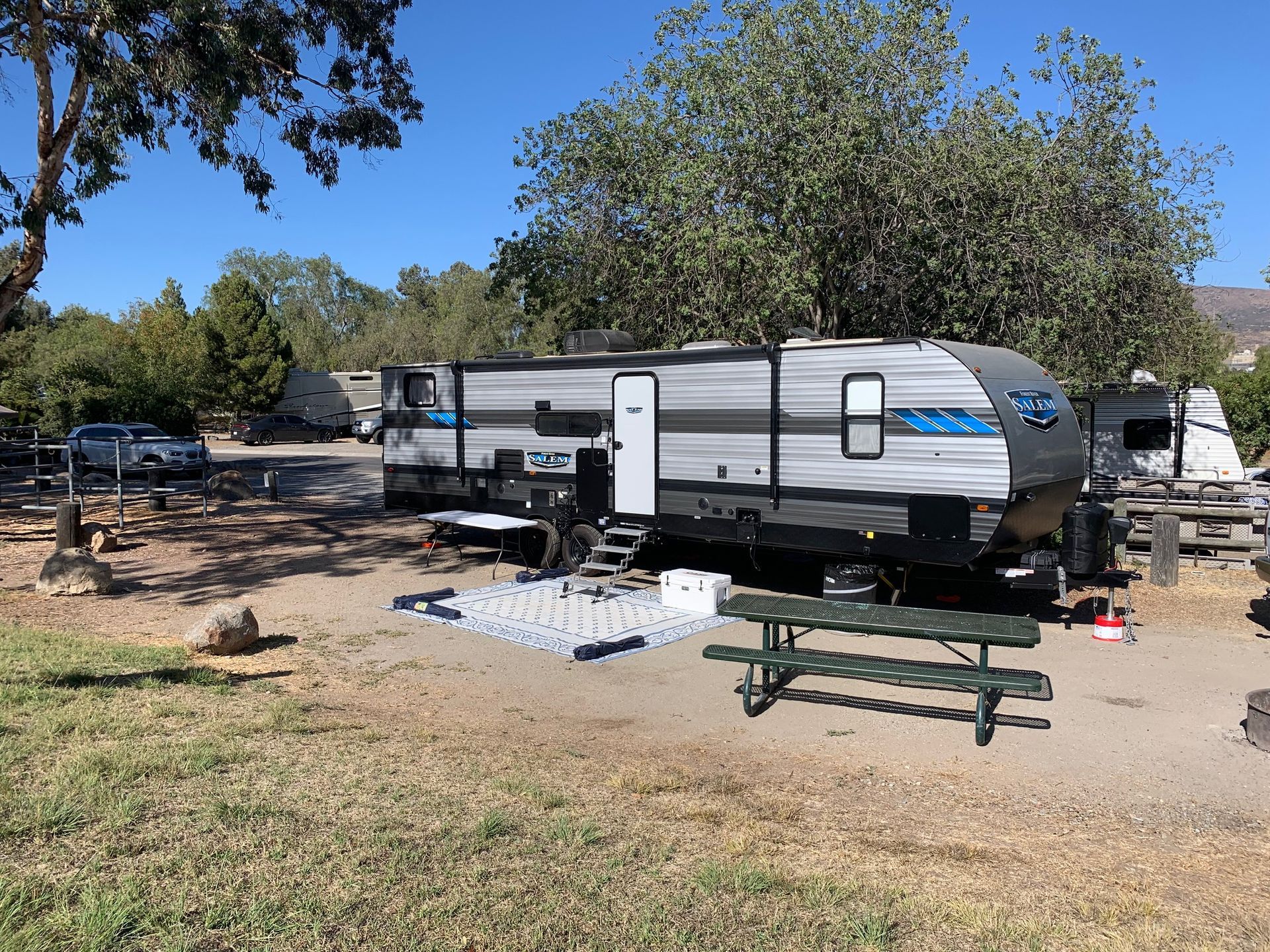 a rv is parked in a grassy area next to a picnic table .