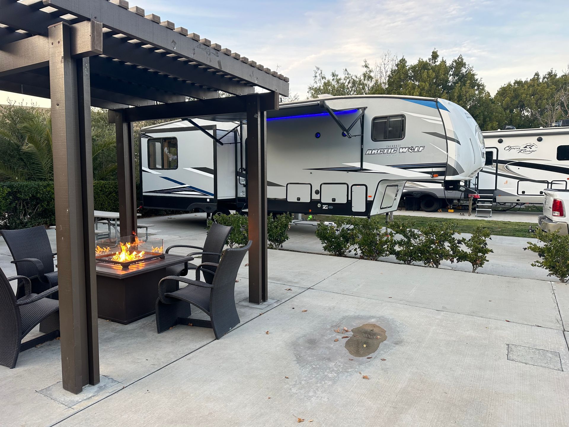 a rv is parked under a pergola next to a fire pit .