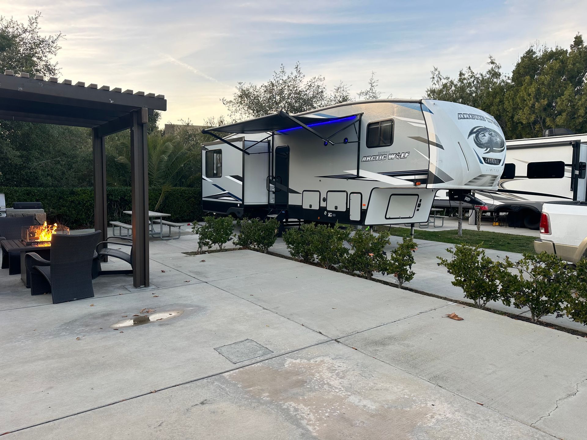A rv is parked in a parking lot next to a fire pit.