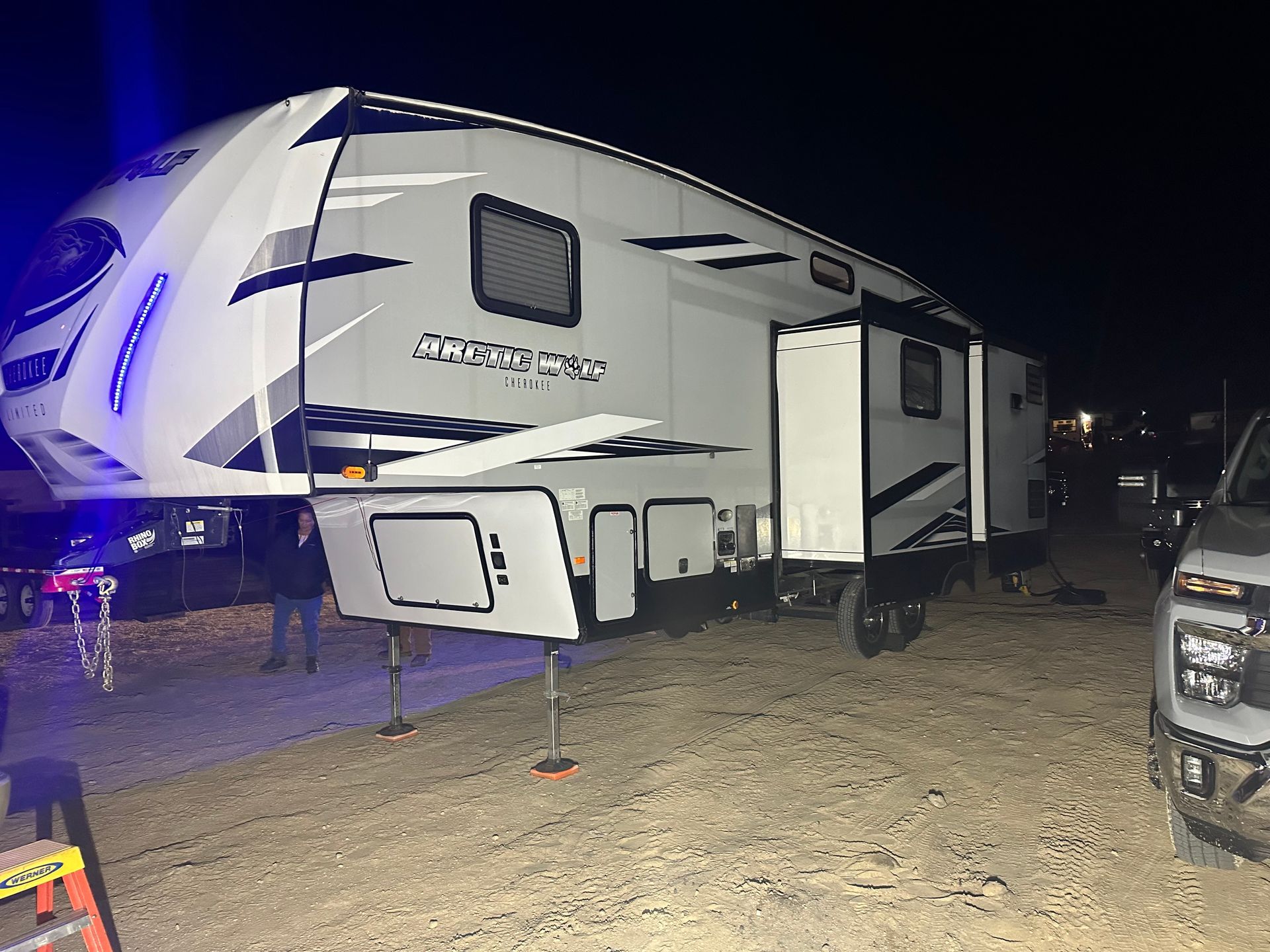 A large white rv is parked in a dirt lot at night.