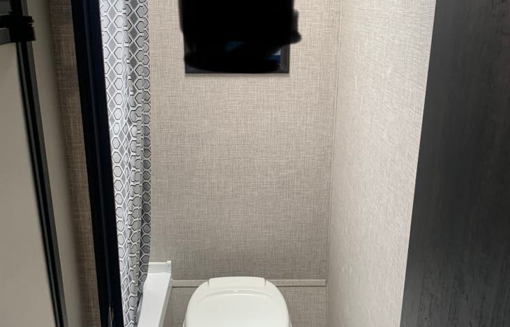 A bathroom with a toilet , shower curtain and mirror.