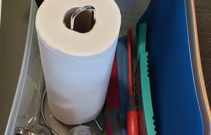 A roll of paper towels is sitting in a drawer next to a cutting board and scissors.