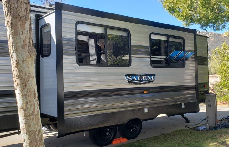 A small trailer is parked next to a tree in a parking lot.