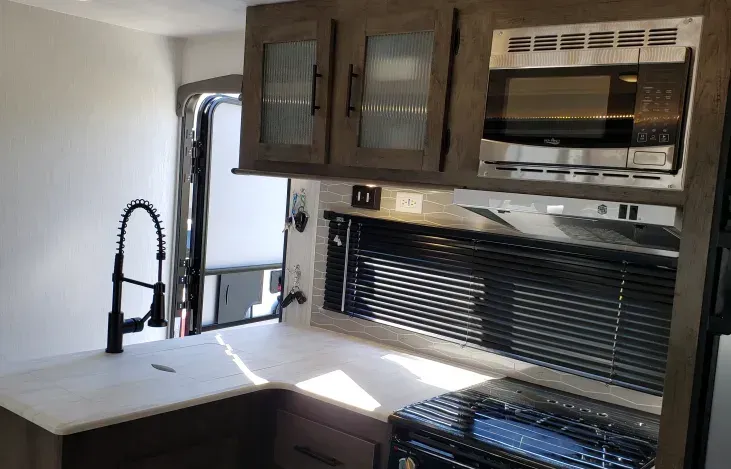 A kitchen in a rv with a sink , stove , microwave and refrigerator.