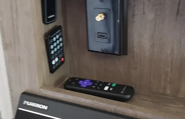 A remote control is sitting on a wooden shelf next to a television.